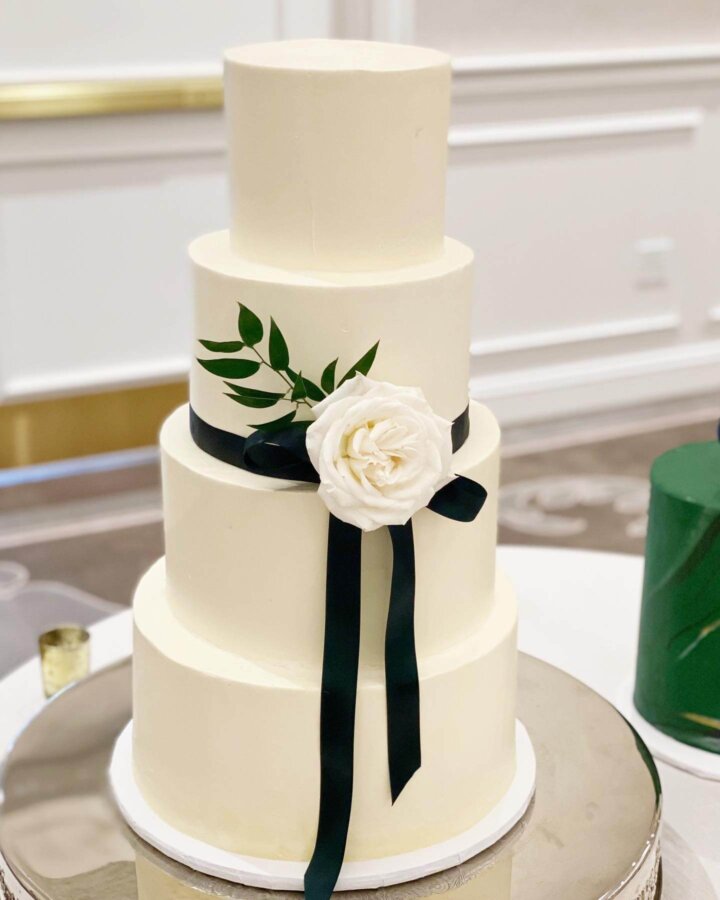Smooth buttercream wedding cake with ribbon and flower. White and emerald green wedding.